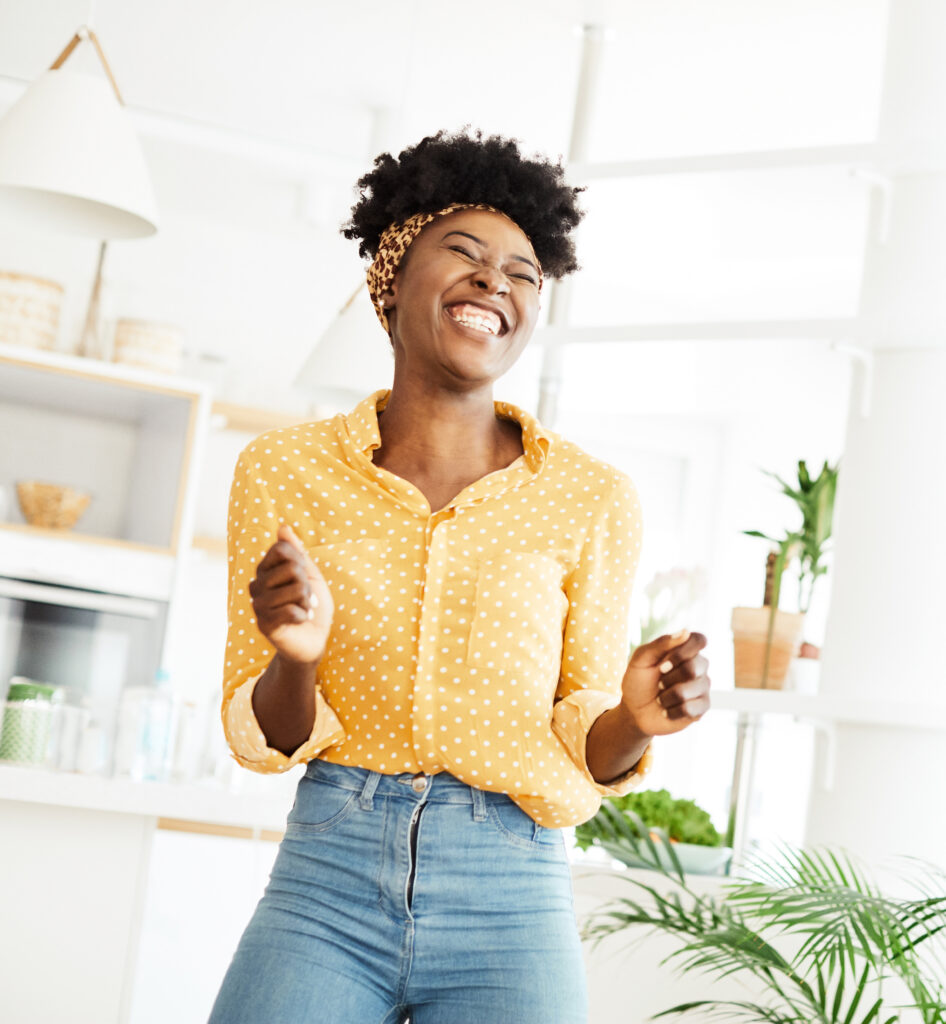 A woman of perimenopausal age with a darker complexion and a short afro of perimenopausal age, smiling happily because she achieved a women’s health and wellness goal